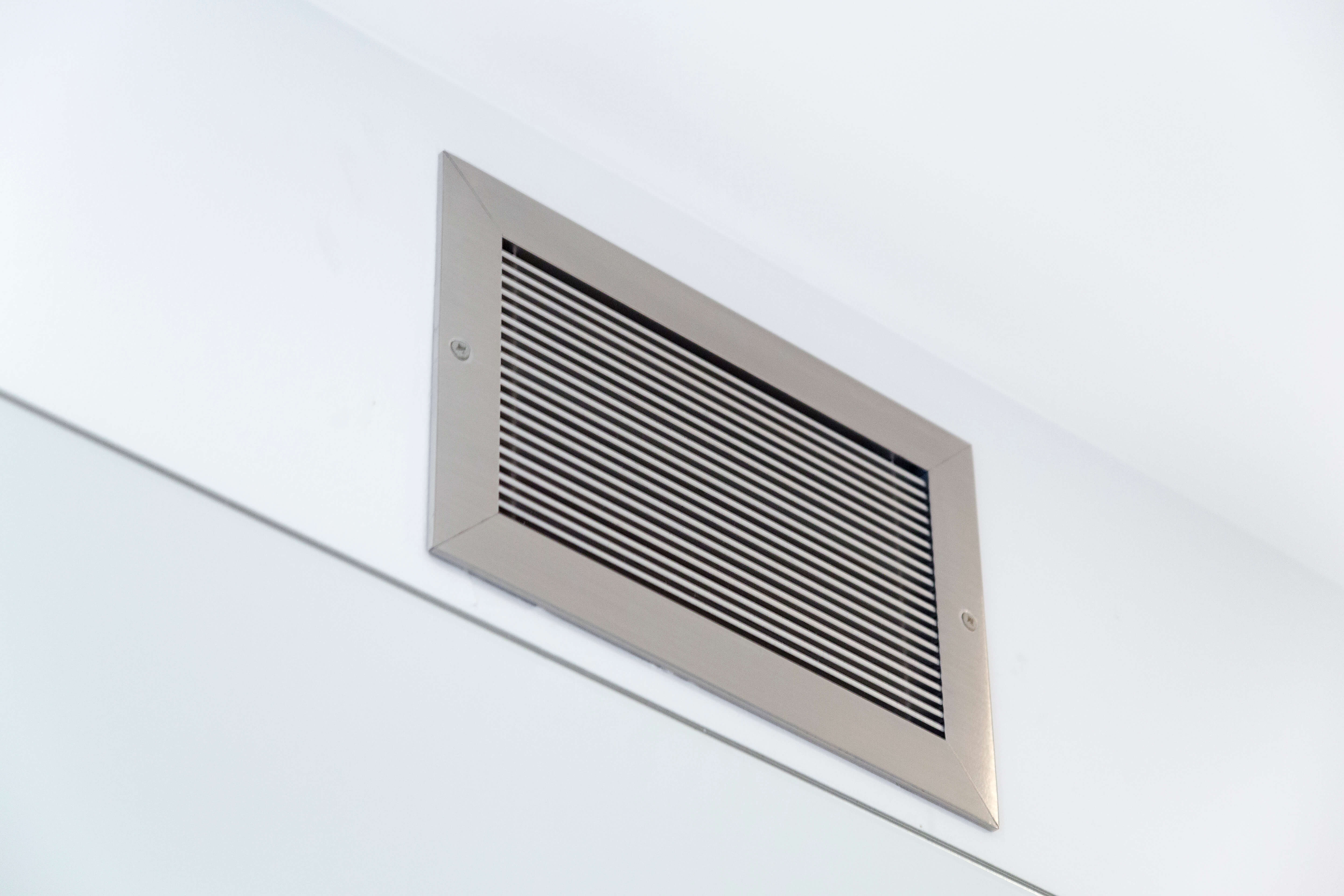 Wall vent cover brushed chrome with screws on white wall