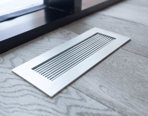 closeup of anodized clear kul grilles vent cover on light grey wood flooring by window
